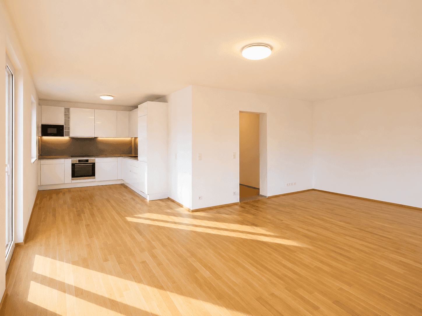 Geräumiger offener Wohnbereich mit Holzboden und integrierter, moderner weißer Küche.