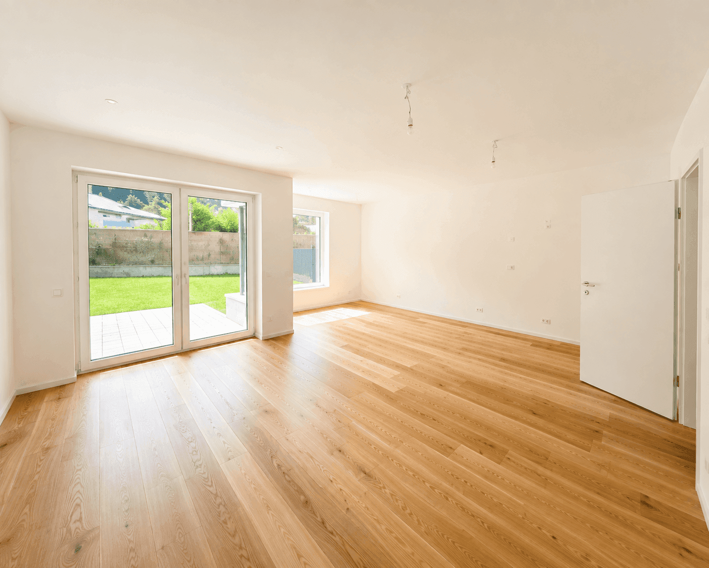 Geräumiges Wohnzimmer mit Holzboden und direktem Zugang zum Garten durch eine große Schiebetür.