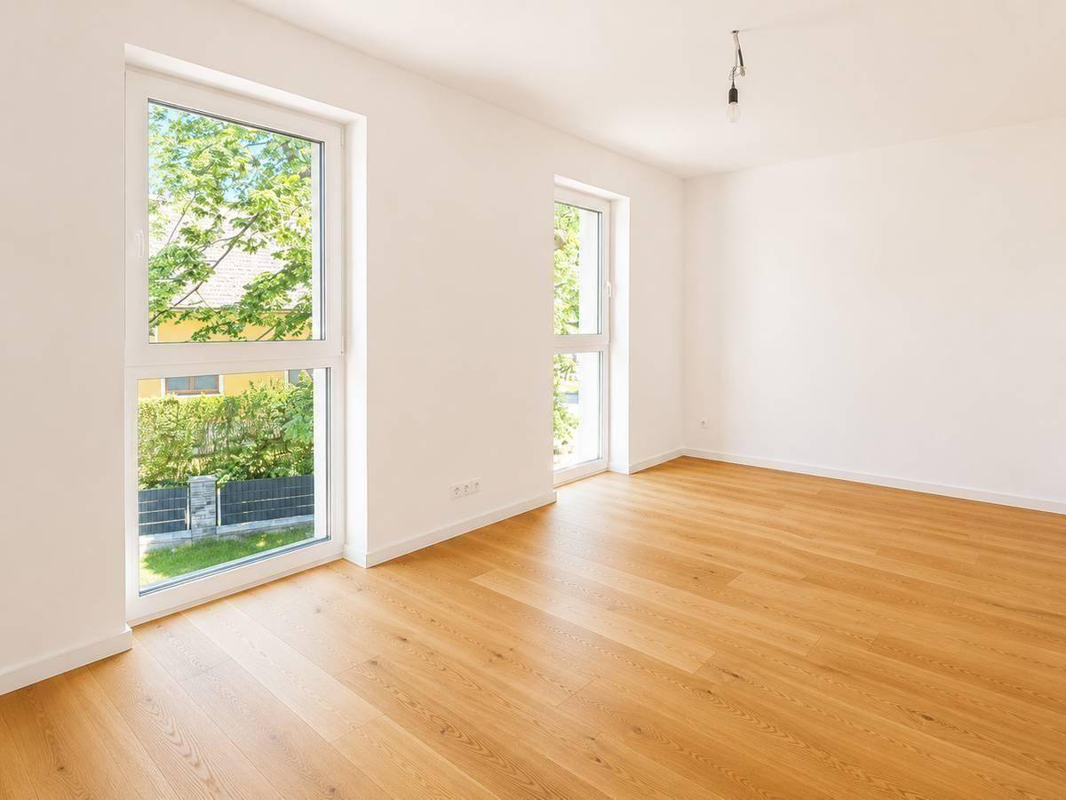 Helles Zimmer mit Parkettboden und großen Fenstern, die viel Tageslicht hereinlassen.