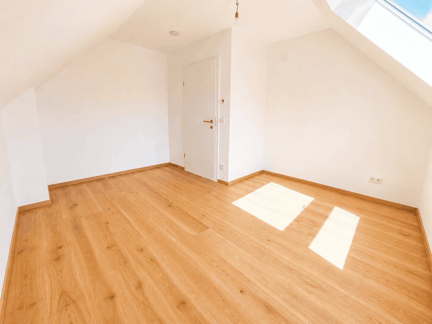 Leeres Zimmer im Dachgeschoss mit hellem Holzfußboden und weiß gestrichenen Wänden, bereit zur individuellen Gestaltung.
