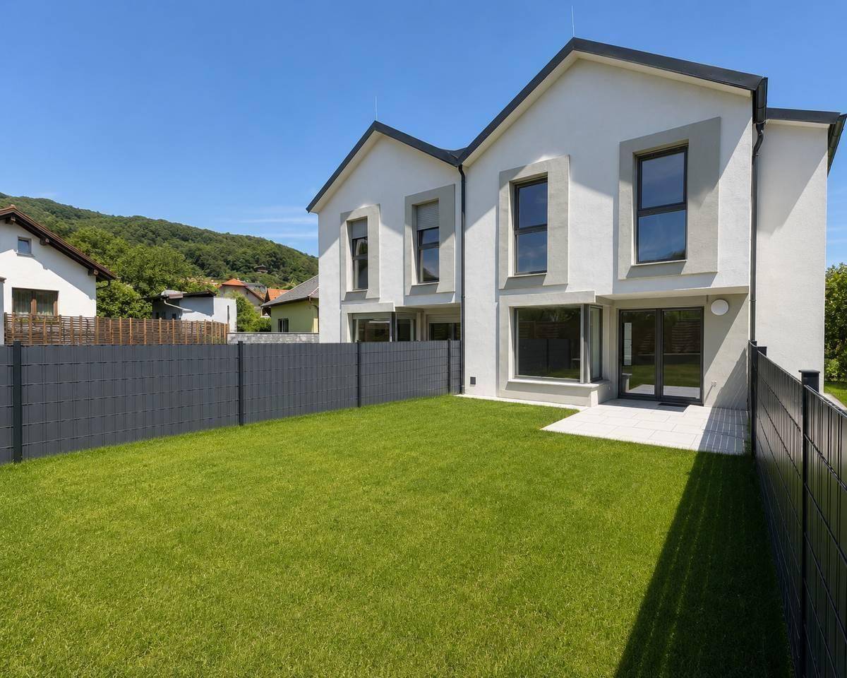 Hinterer Gartenbereich mit Rasenfläche und kleiner Terrasse, umgeben von einem modernen Zaun.
