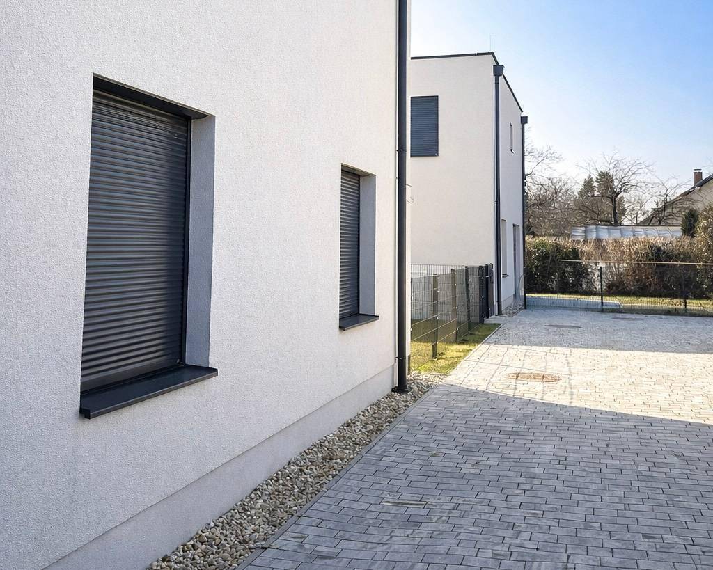 Seitenansicht eines modernen Hauses mit gepflasterter Auffahrt und geschlossenen Rollläden.
