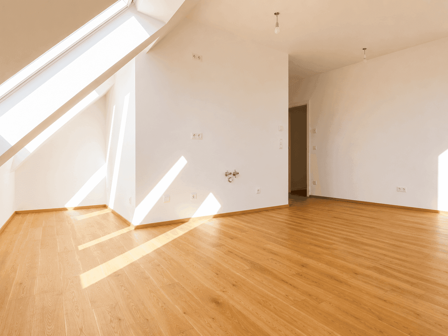 Lichtdurchfluteter Dachgeschossraum mit schrägen Wänden, Holzboden und großen Dachfenstern.