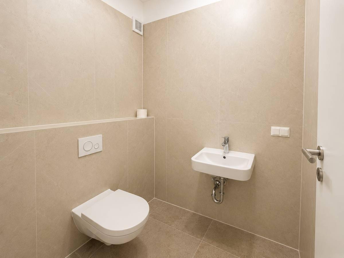 Helles Gäste-WC mit wandhängender Toilette, Waschbecken und beigefarbenen Fliesen.