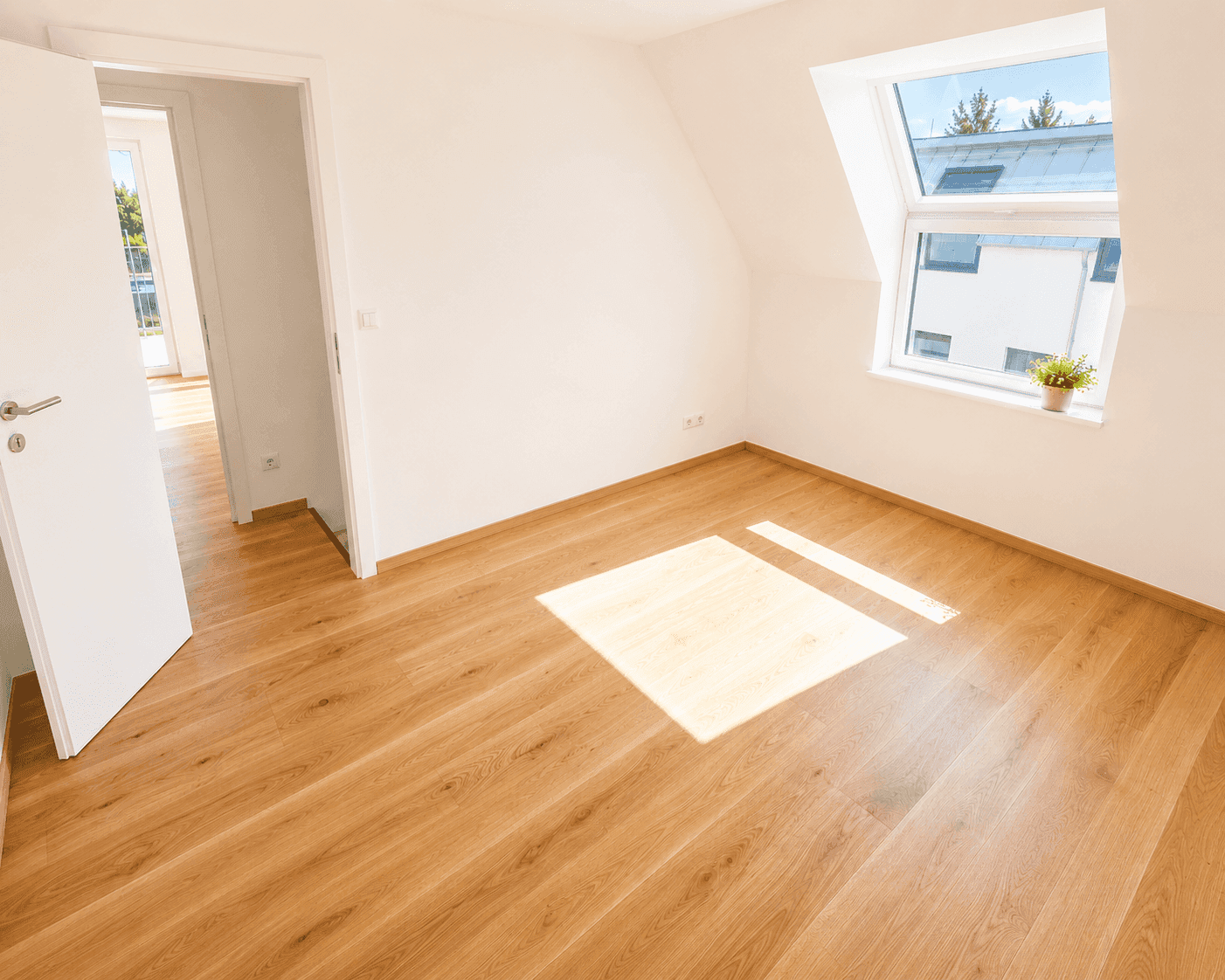 Lichtdurchflutetes Dachgeschosszimmer mit hellem Holzfußboden und großem Fenster, das viel Sonnenlicht hereinlässt.
