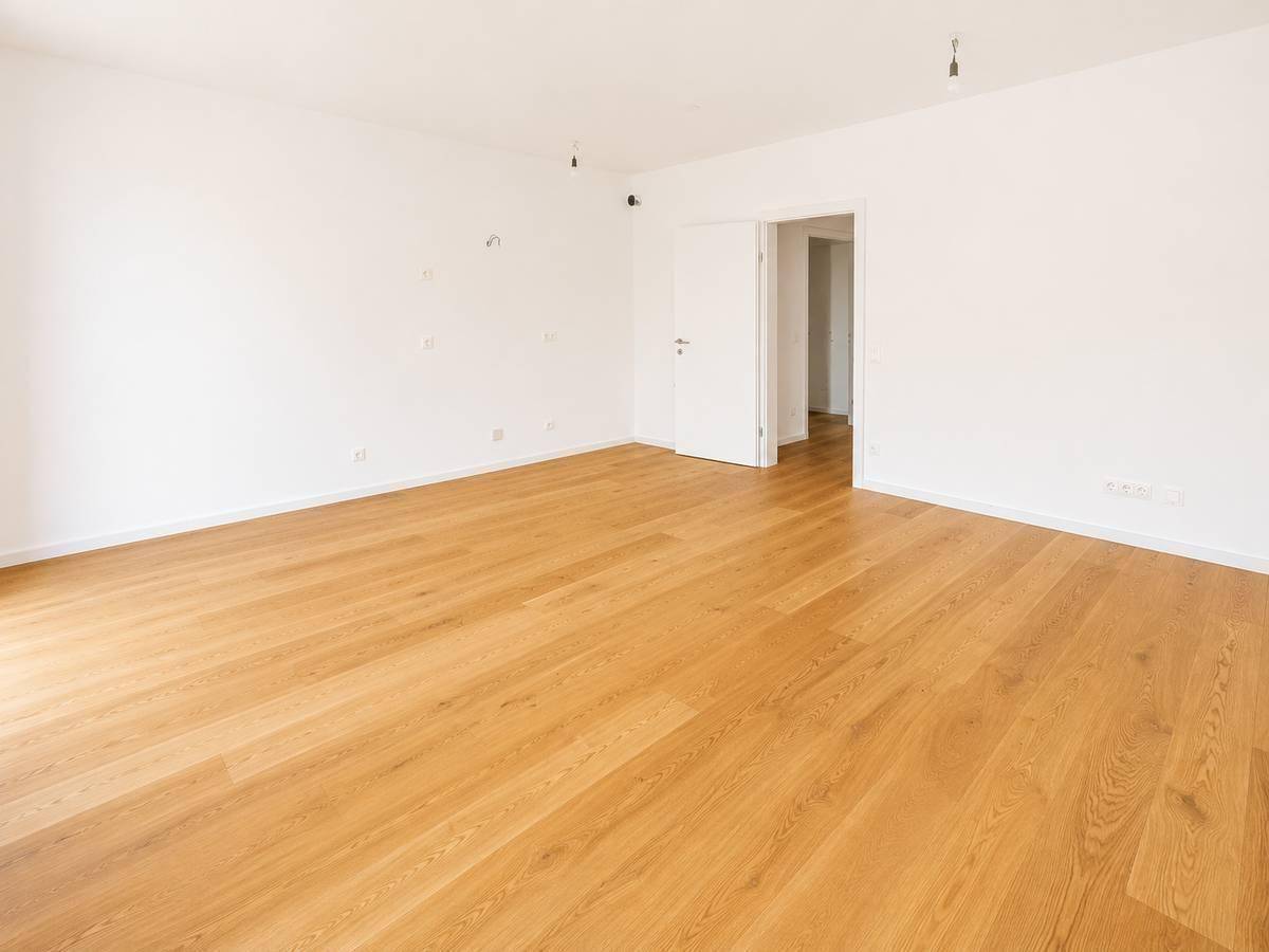 Geräumiger, heller Wohnraum mit Parkettboden und weiß gestrichenen Wänden.
