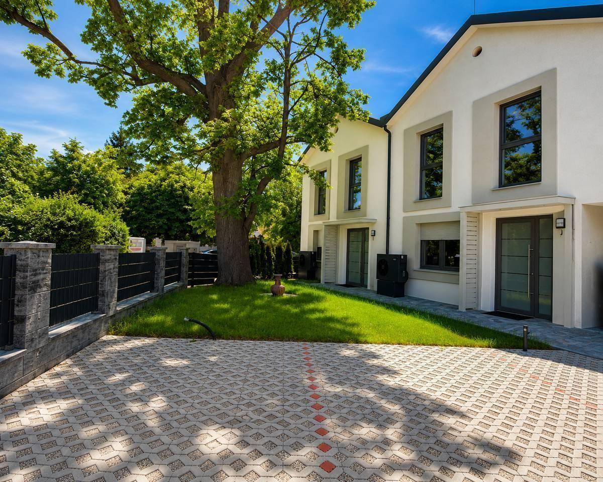 Vorderansicht der Reihenhäuser mit großem Baum, gepflastertem Vorplatz und moderner Zaunanlage.