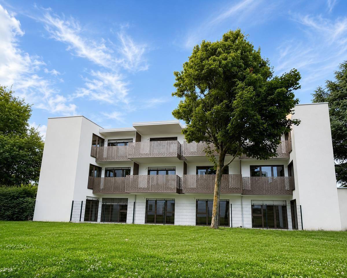 Modernes Mehrfamilienhaus mit Balkonen und gepflegter Grünfläche unter blauem Himmel.