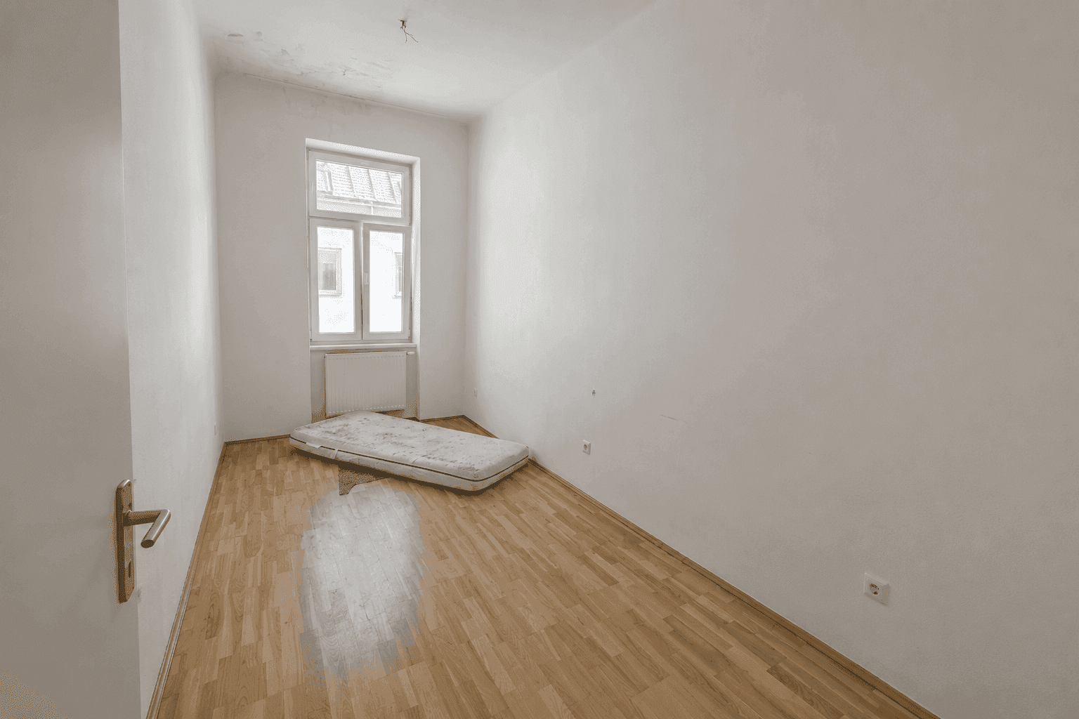 Einfaches Schlafzimmer mit Holzboden und einem Fenster, bereit zur individuellen Gestaltung.