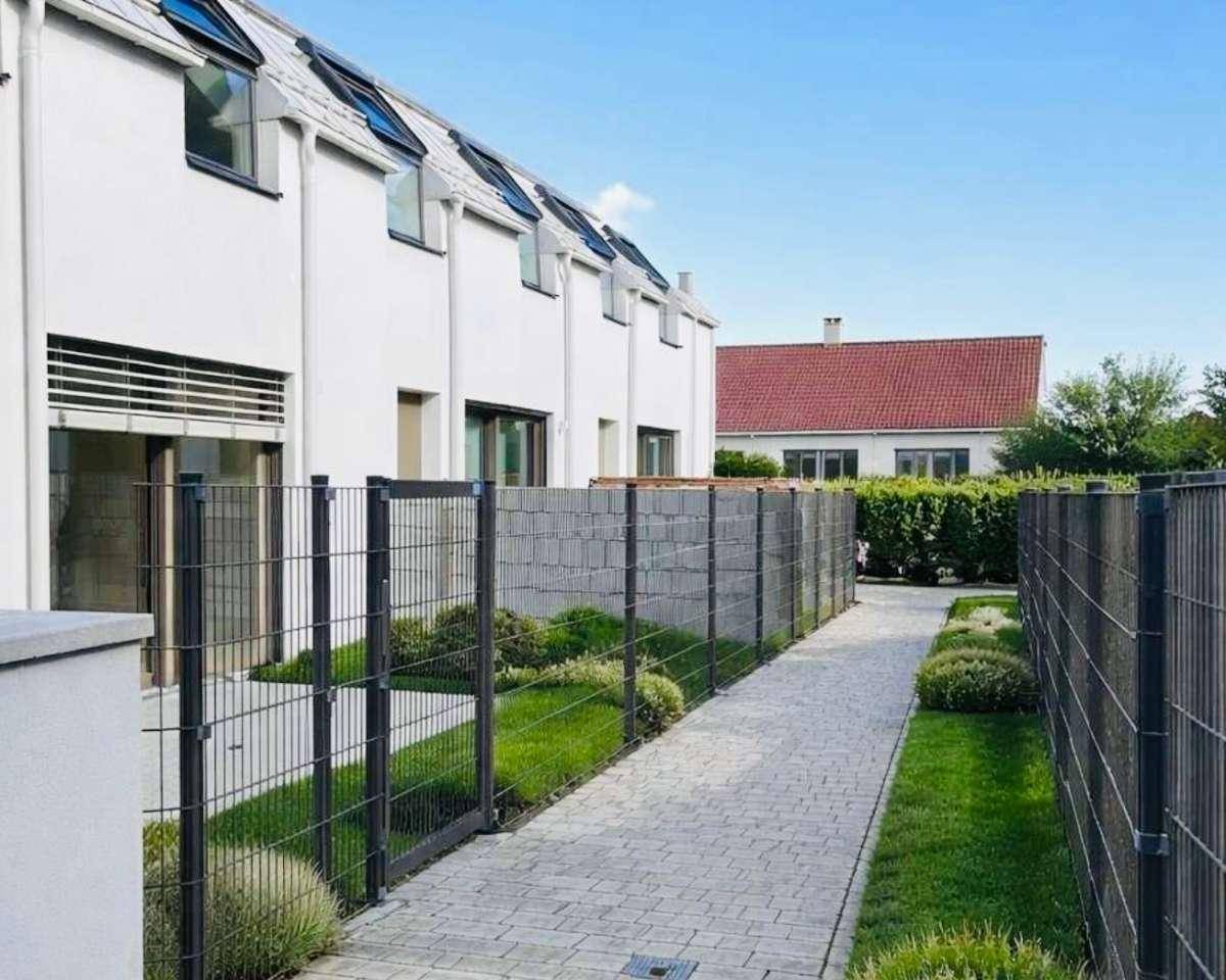 Seitenansicht der modernen Gebäude mit gepflastertem Weg, kleinen Grünflächen und hohen Zäunen.