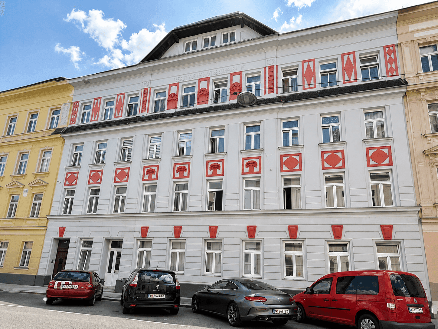 Historisches Gebäude mit auffälliger Fassadengestaltung, vielen Fenstern und parkenden Autos davor.