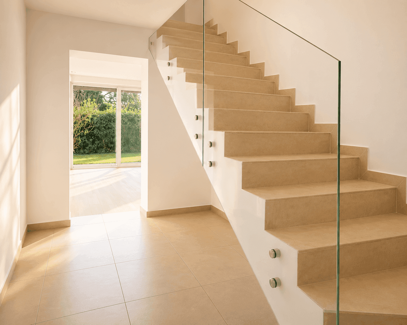 Lichtdurchfluteter Flur mit Treppe, Glasgeländer und Blick in den Garten durch große Fenster.