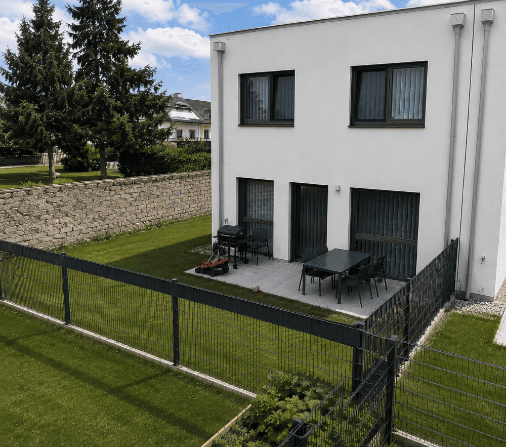 Gemütliche Terrasse mit Gartenmöbeln und Grillbereich, umgeben von einer Steinmauer und Rasen.