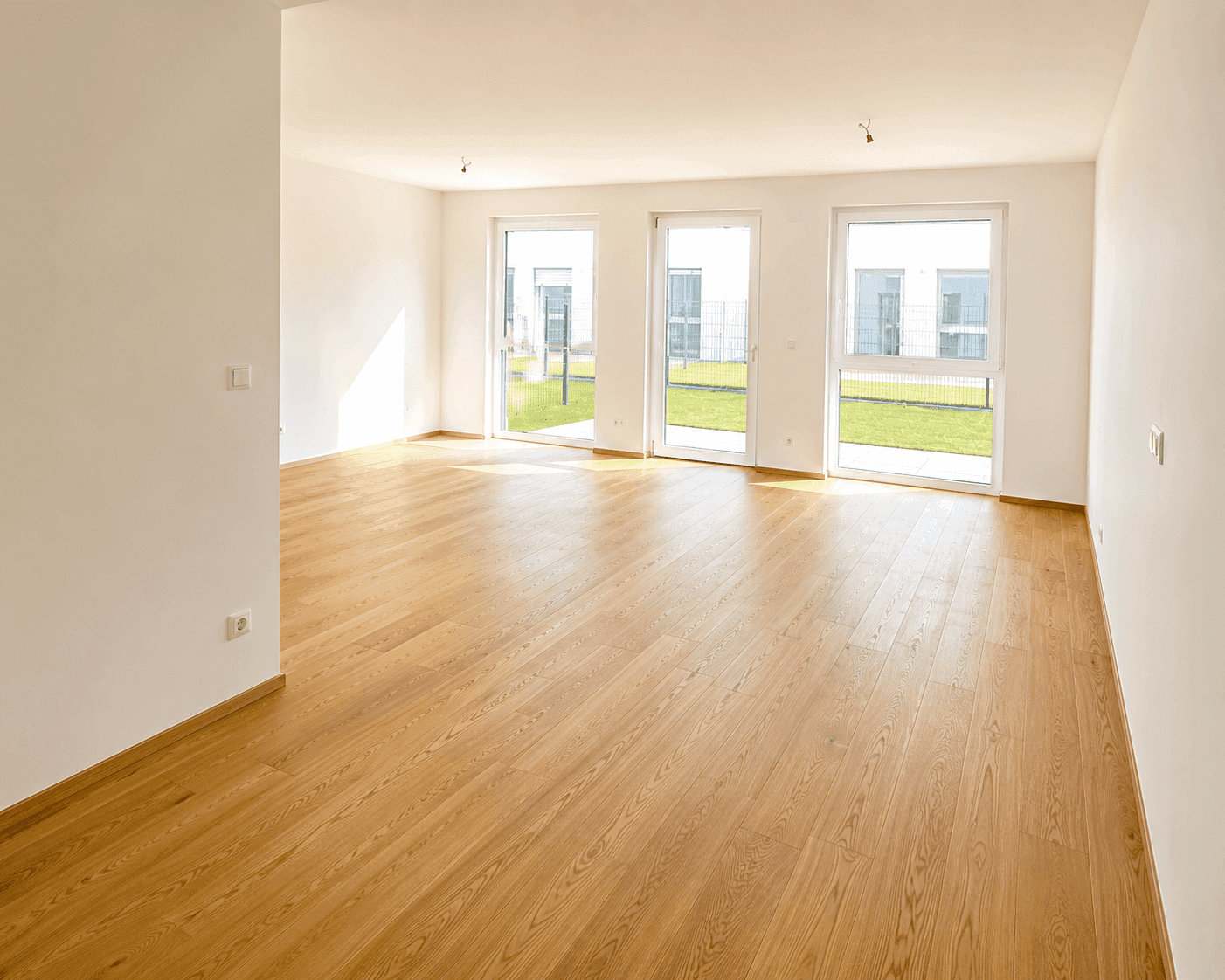 Geräumiges, leeres Wohnzimmer mit Eichenparkett und großen Fenstern zum Garten.