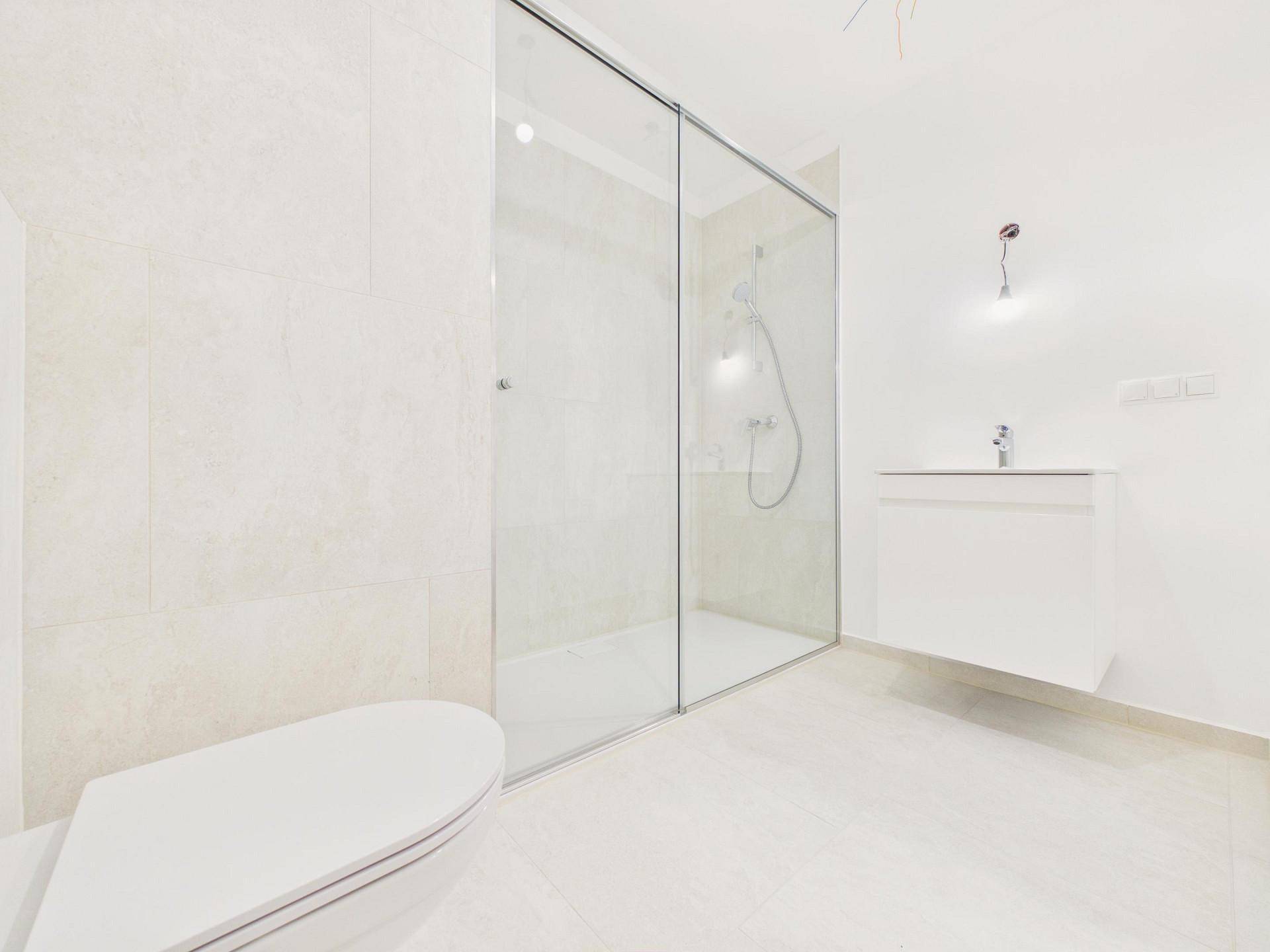 Helles Badezimmer mit großer Duschkabine aus Glas und modernem Waschbeckenunterschrank.