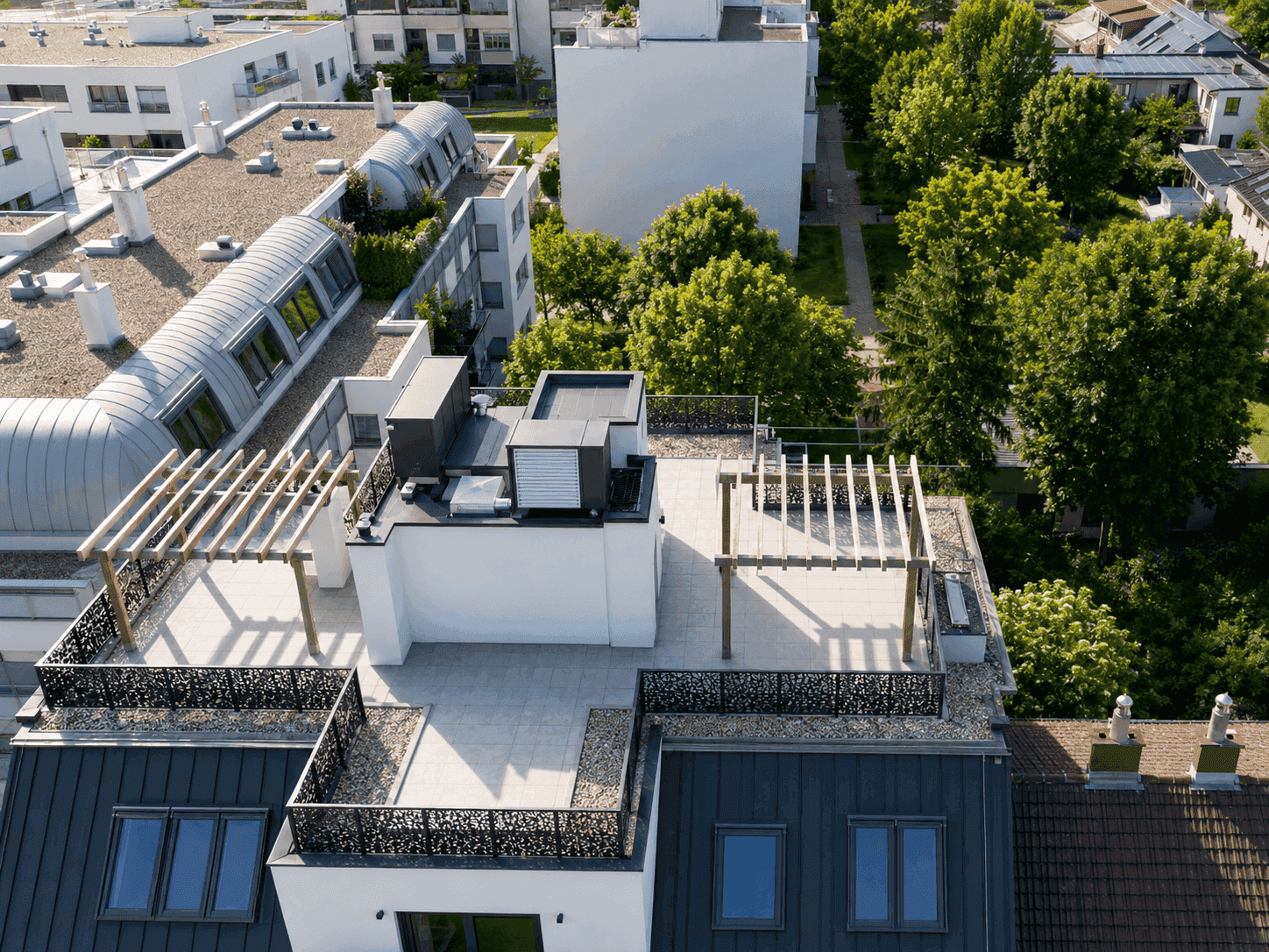 Dachlandschaft eines modernen Gebäudes mit Dachterrassen und grünen Bäumen.