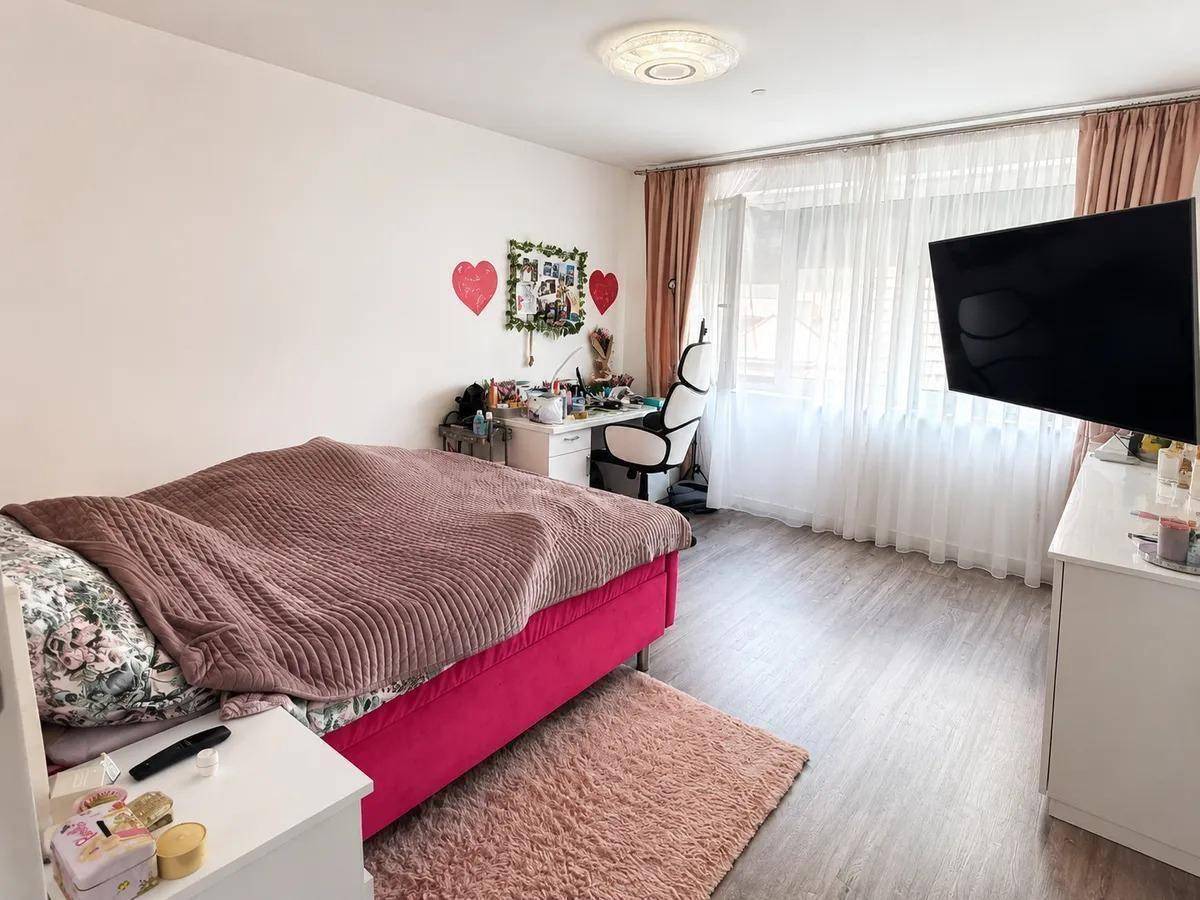 Helles Kinder- oder Gästezimmer mit rosa Bett, Schreibtisch und großem Fenster.