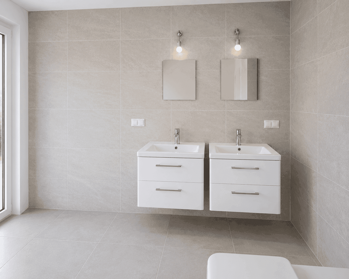 Modernes Badezimmer mit hellgrauen Fliesen, zwei Waschbecken und Spiegelschränken.