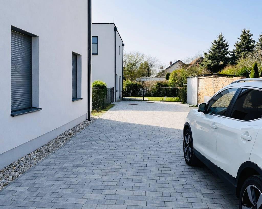 Seitenansicht eines modernen Hauses mit gepflasterter Auffahrt und grüner Umgebung.
