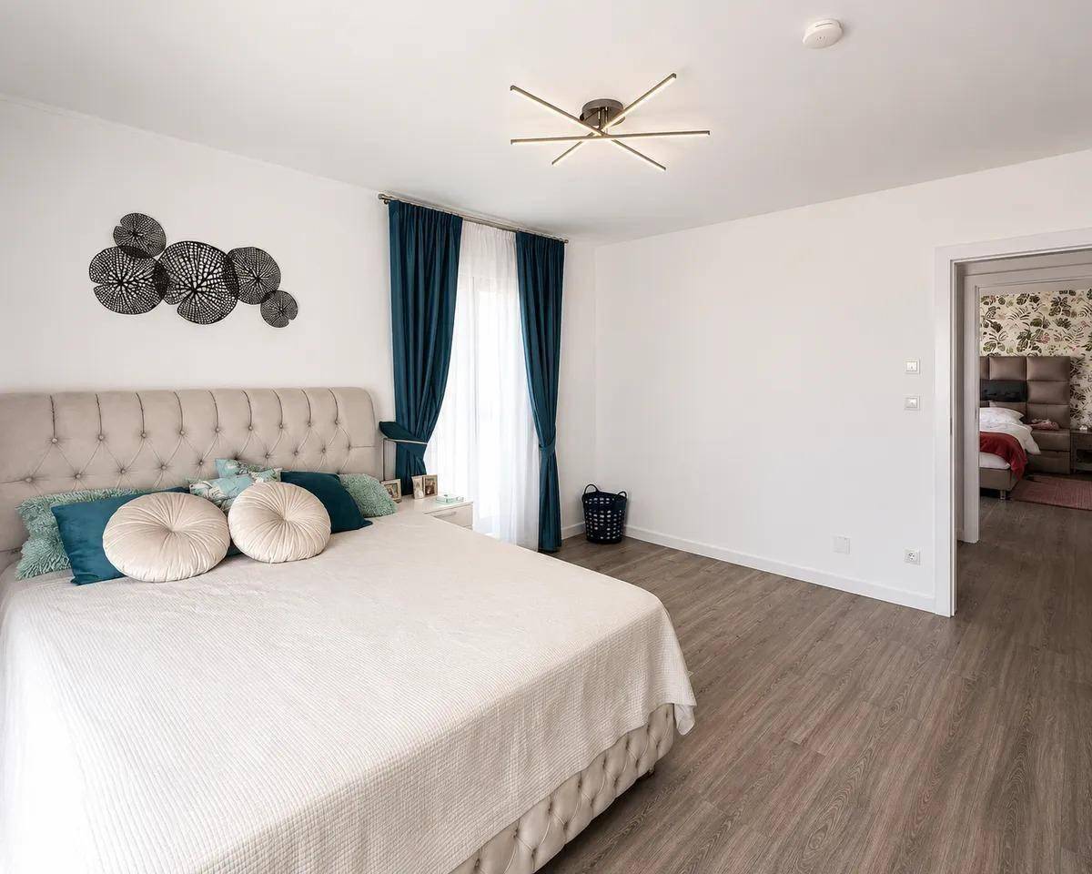 Gemütliches Schlafzimmer mit großem Bett, Laminatboden und dekorativen Wandelementen.