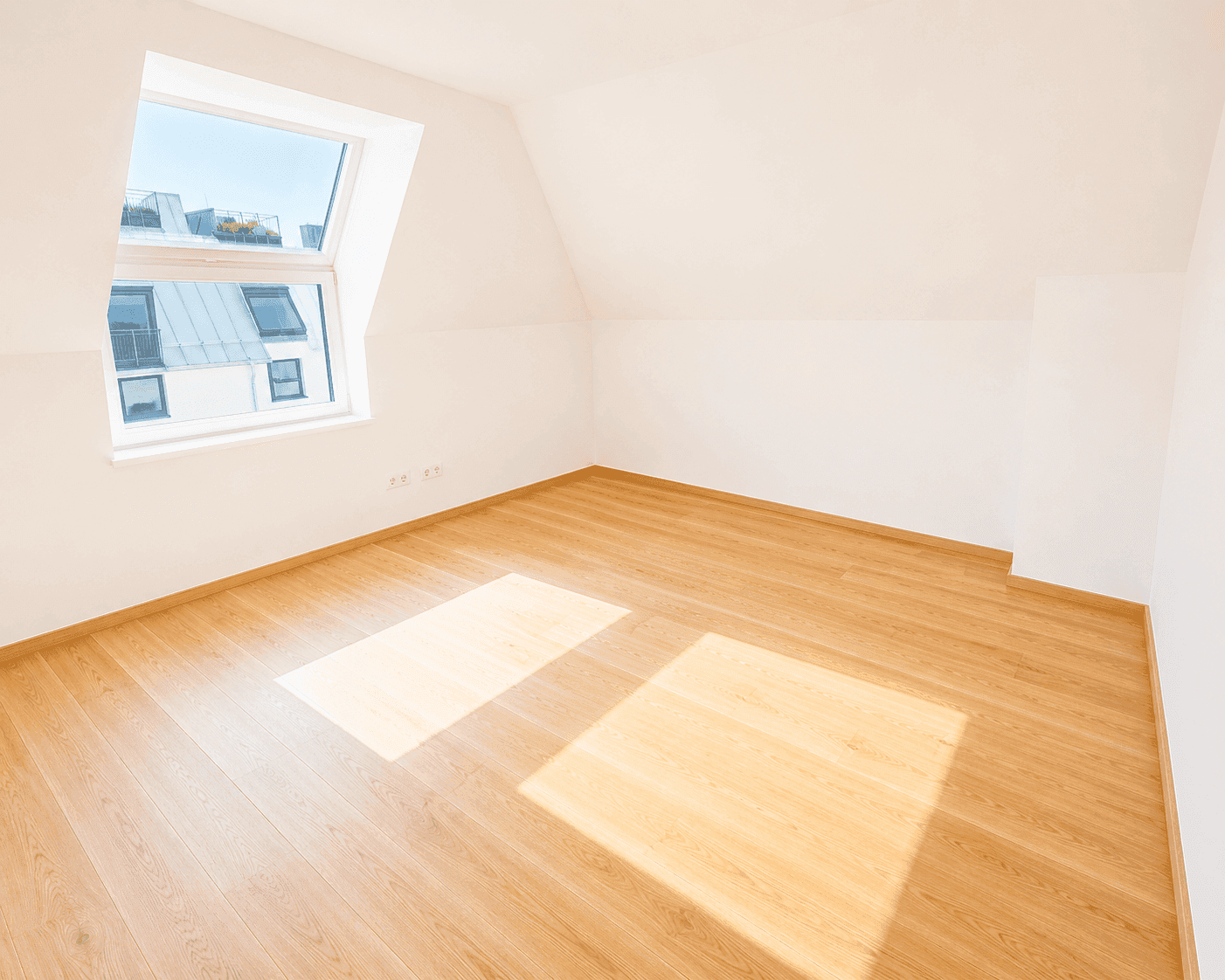 Geräumiges Dachgeschosszimmer mit hellem Holzfußboden und schrägem Dach, ideal für ein gemütliches Schlafzimmer.