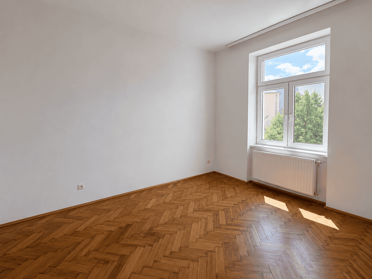 Helles Schlafzimmer mit Fischgrätparkett und großem Fenster mit Blick ins Grüne.