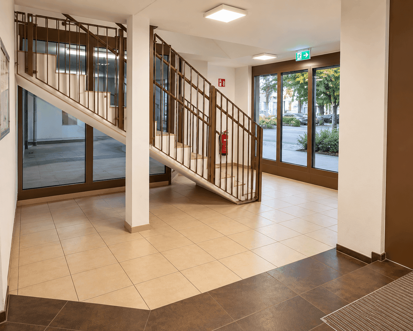 Heller Treppenaufgang in einem Mehrfamilienhaus mit großen Fenstern und Fliesenboden.