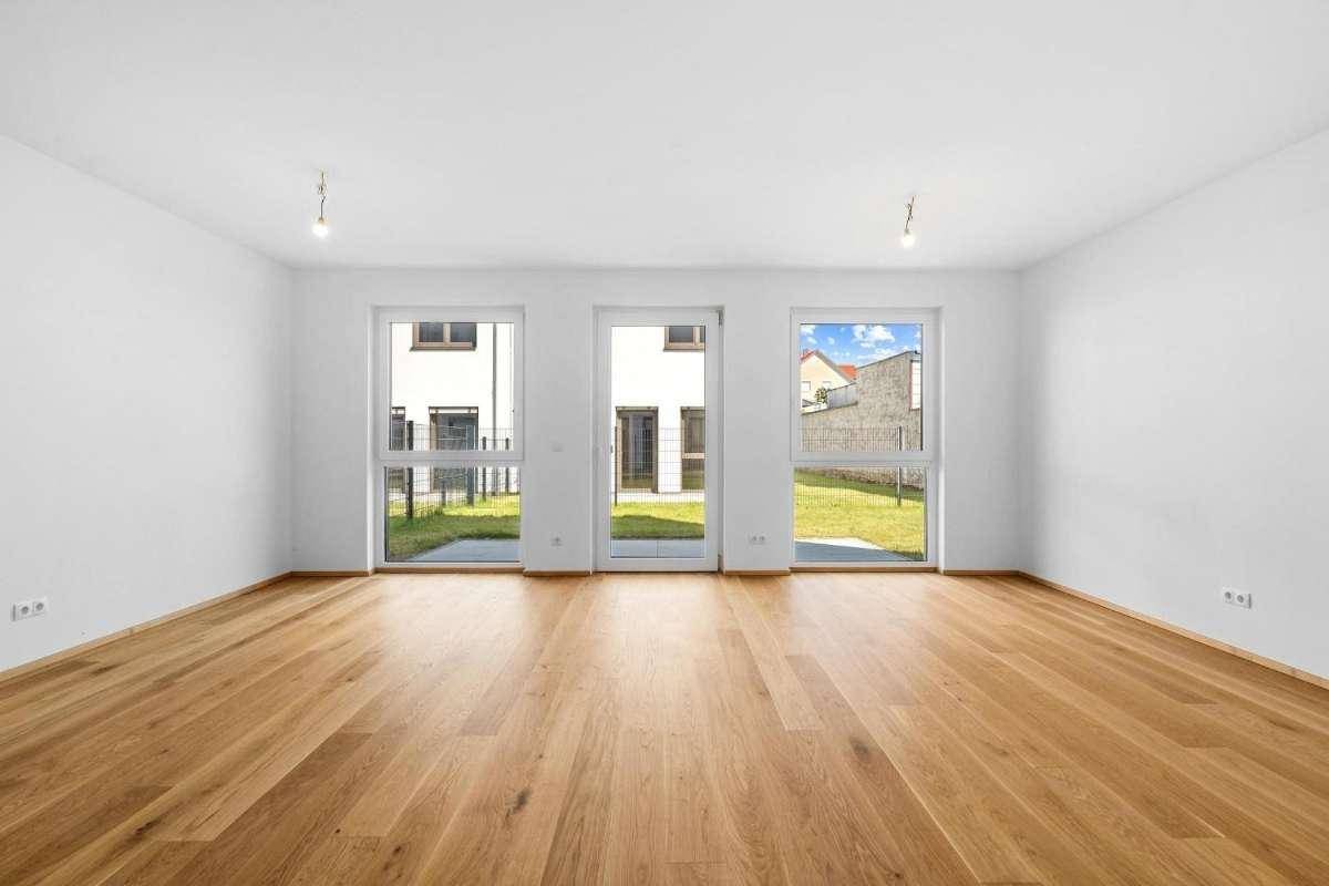 Helles, leeres Wohnzimmer mit Eichenparkett und großen Fenstern zum Garten.