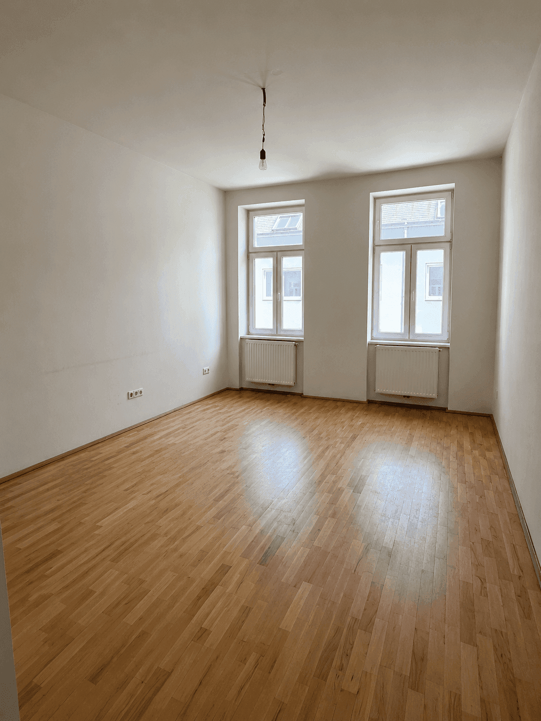 Helles Schlafzimmer mit Fischgrätparkett und zwei großen Fenstern für viel Tageslicht.
