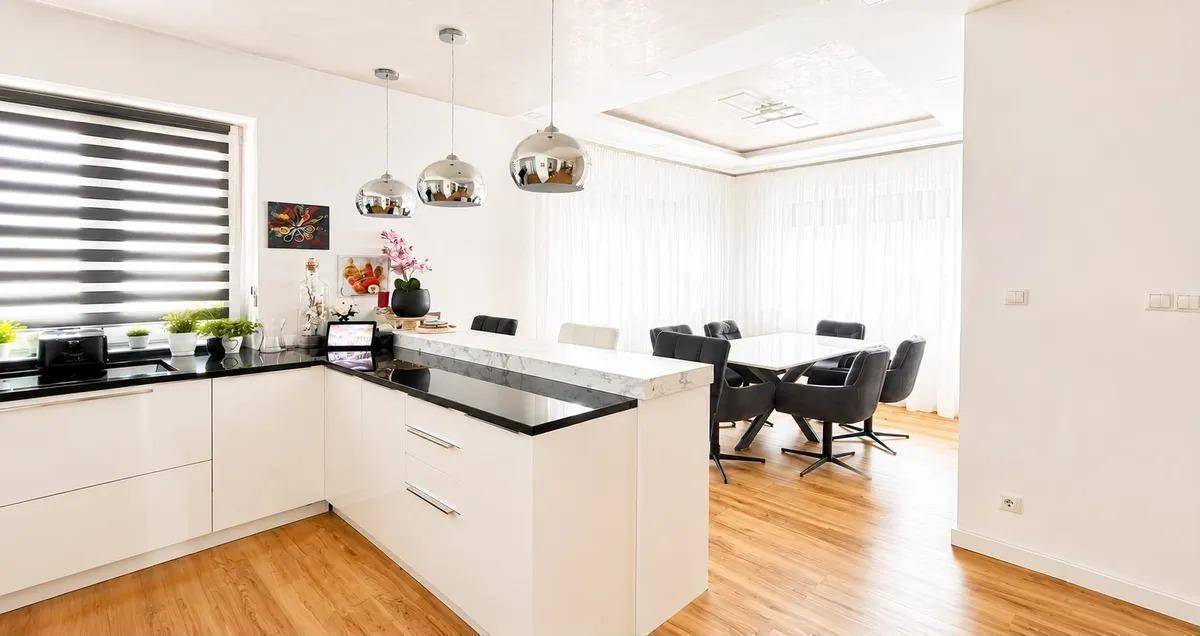 Heller Wohn- und Essbereich mit integrierter Küche, Laminatboden und eleganten Deckenleuchten.