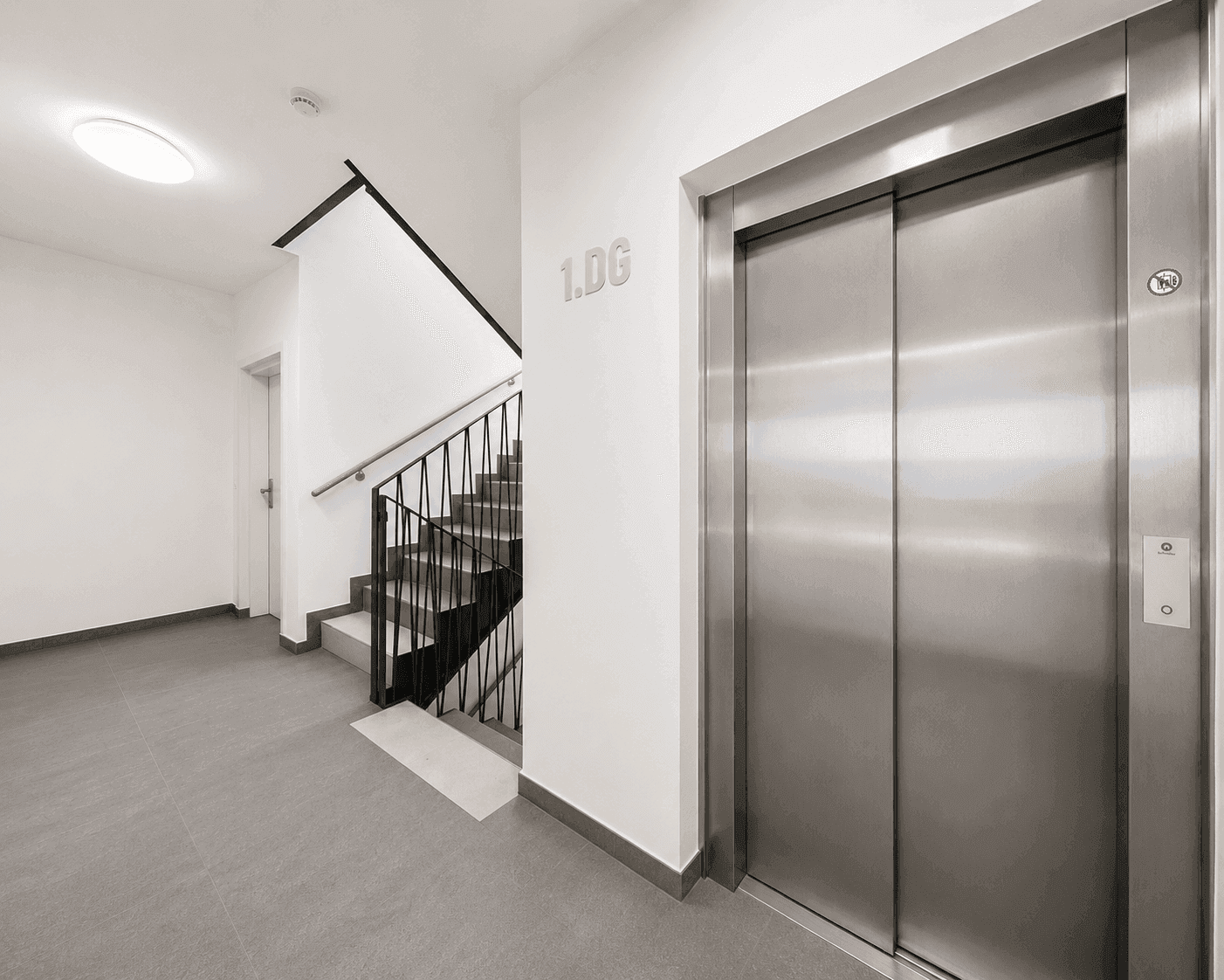 Heller Flur im Gebäude mit modernem Aufzug und Treppenhauszugang.