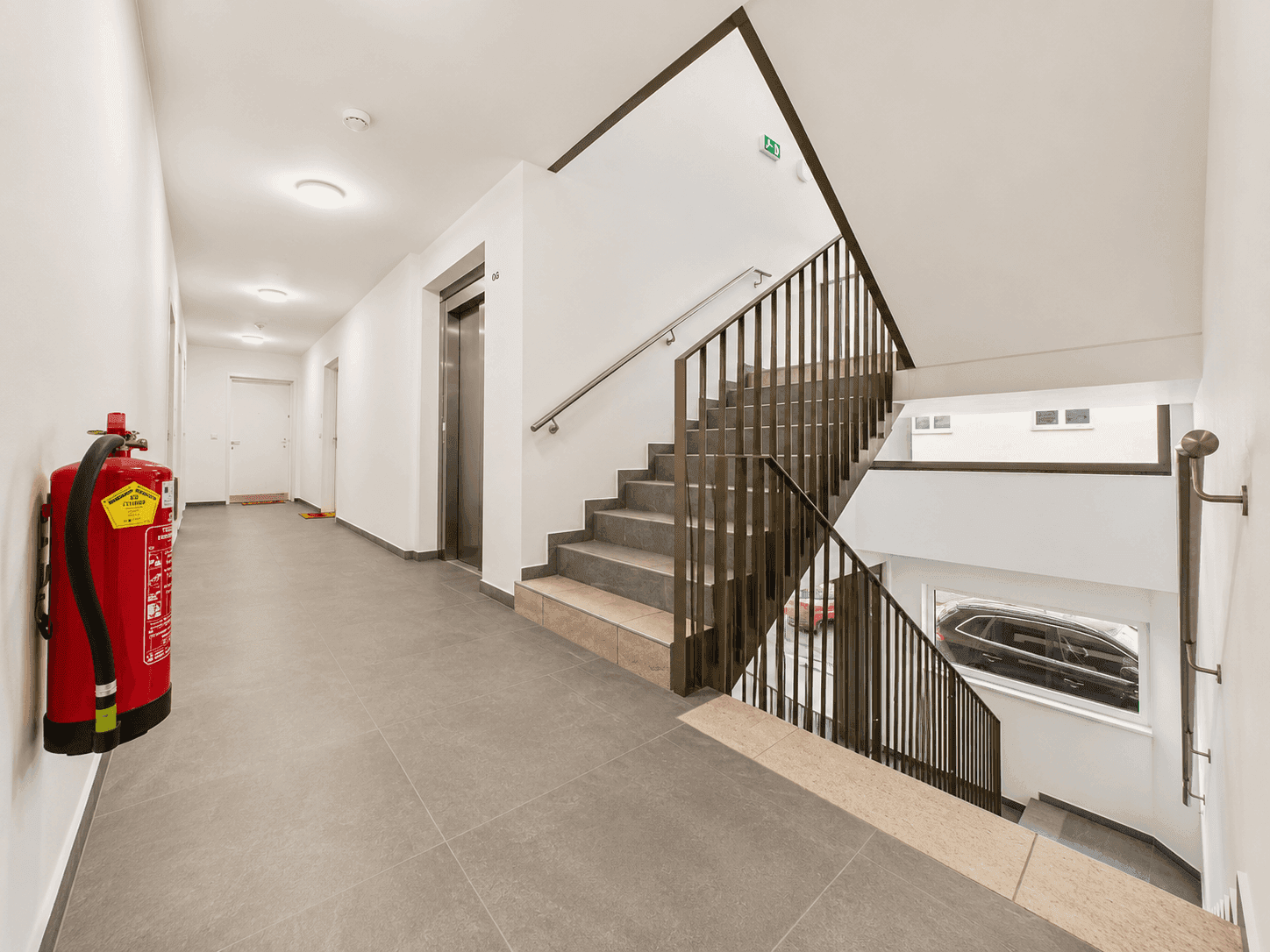 Moderner Eingangsbereich mit Treppe, Aufzug und Fliesenboden in einem Mehrfamilienhaus.