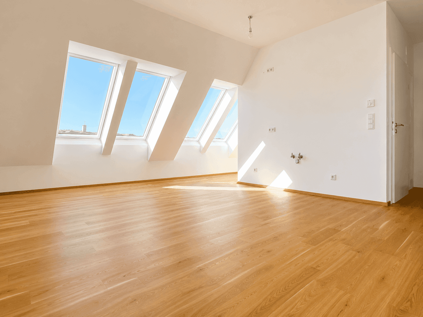 Heller Dachgeschossraum mit schrägen Wänden, großen Dachfenstern und neuem Holzfußboden.