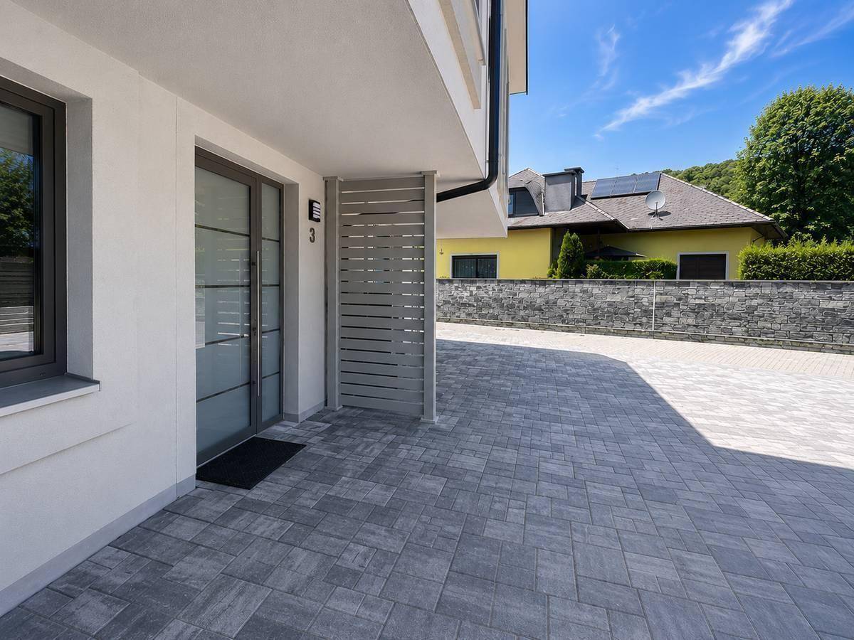 Moderner Eingangsbereich einer Doppelhaushälfte mit gepflastertem Vorplatz und Hausnummer.