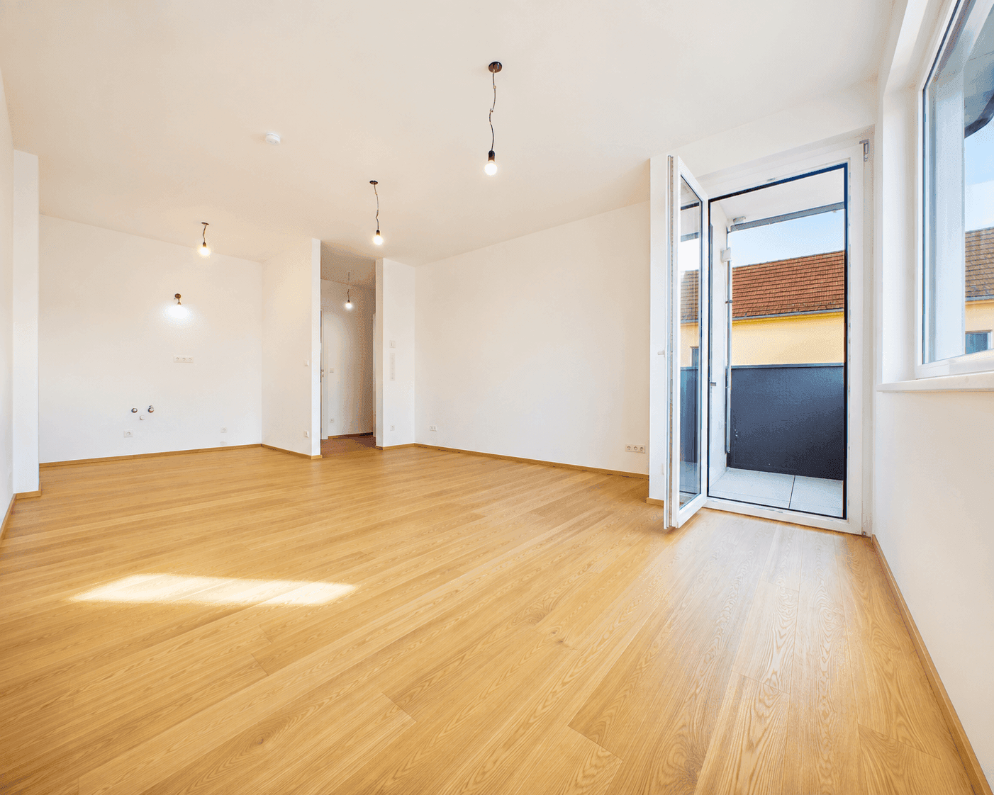 Lichtdurchfluteter Raum mit Holzboden und Zugang zu einem Balkon, ideal für Wohn- oder Schlafbereich.