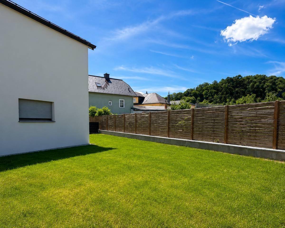 Seitlicher Gartenbereich mit Rasenfläche und Holzzaun, bietet Privatsphäre und Grün.