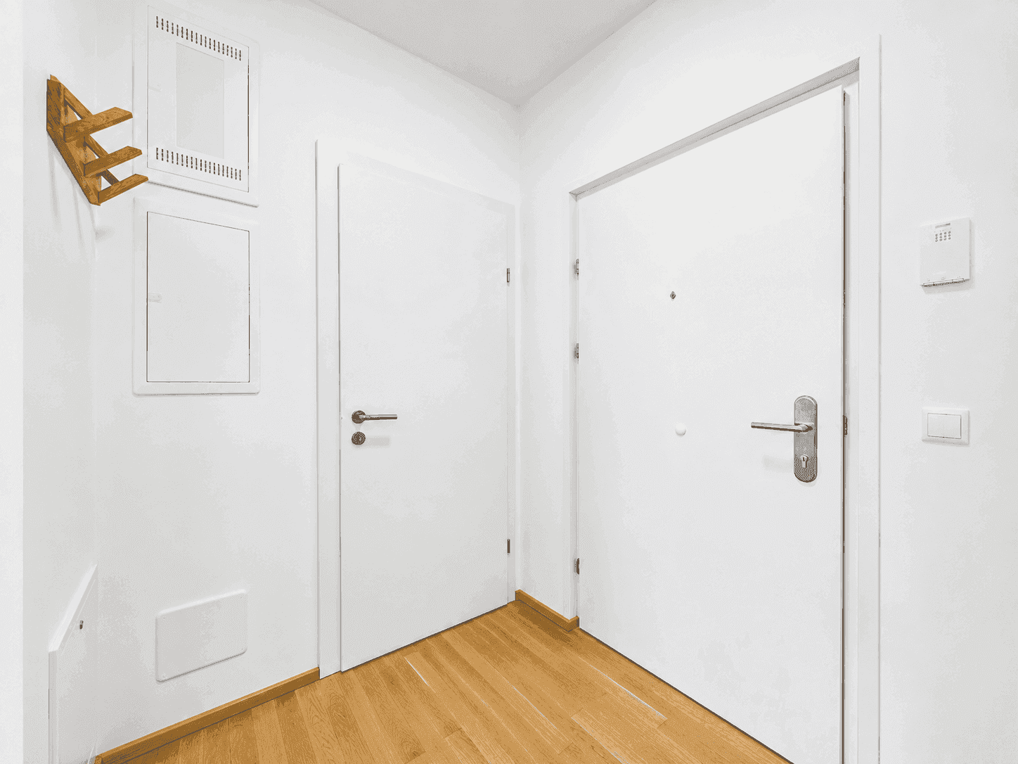 Heller Eingangsbereich mit Holzboden, weißen Türen und einer praktischen Garderobe.