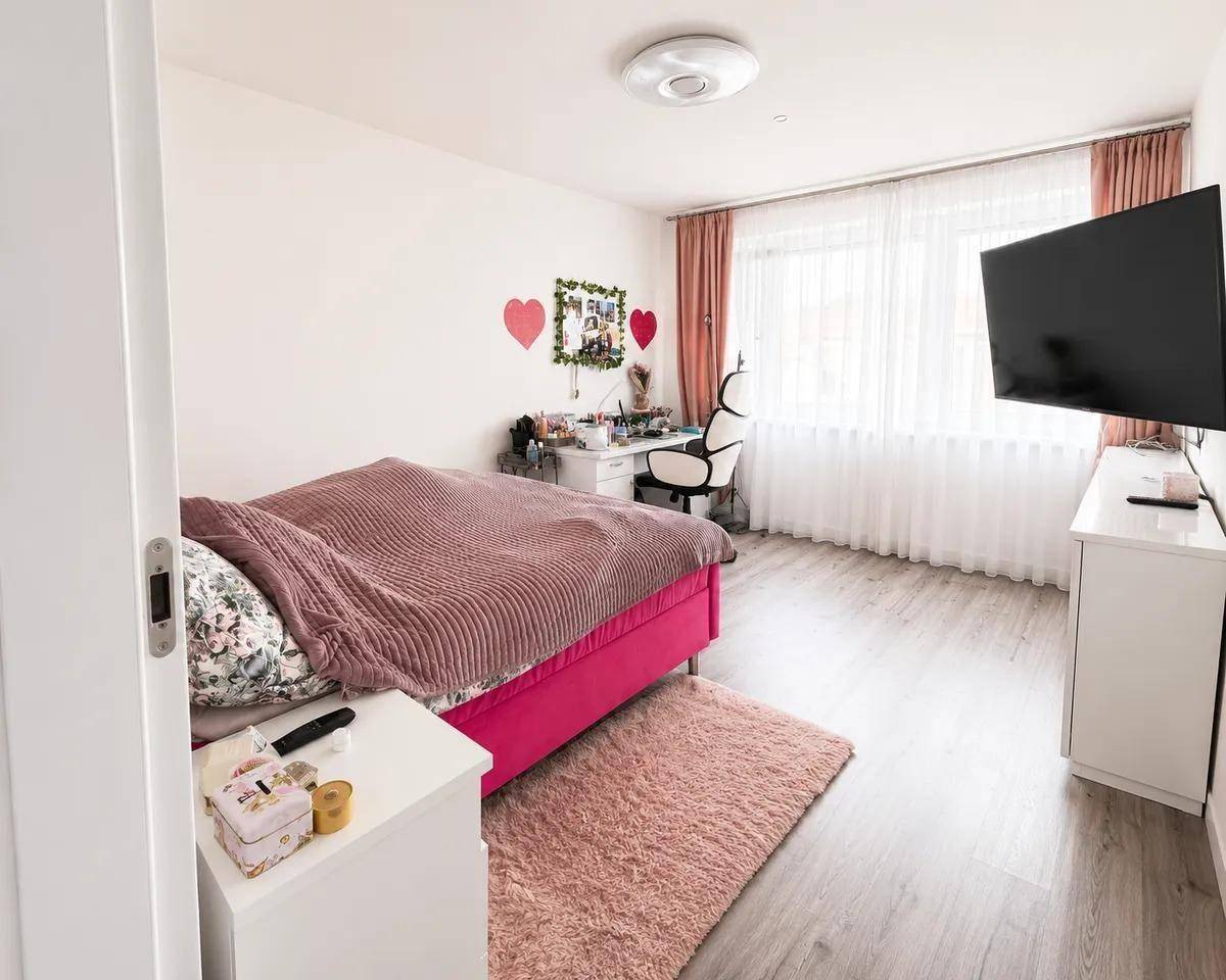 Helles Kinder- oder Gästezimmer mit rosa Bett, Schreibtisch und großem Fenster.
