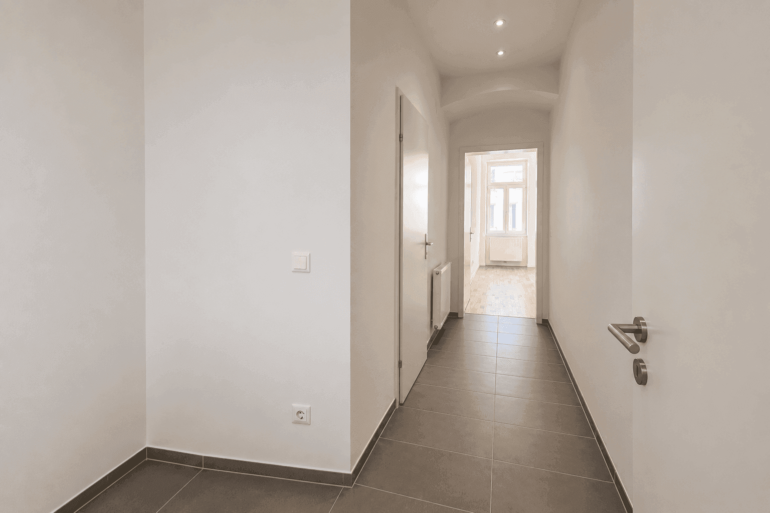 Heller Flur mit modernen grauen Fliesen und Zugang zu weiteren Räumen der Wohnung.