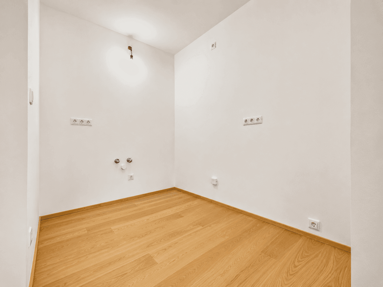 Leerer Raum mit Holzboden und Anschlüssen an der Wand, ideal für eine Küche oder Waschküche.