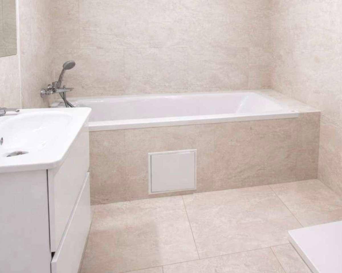 Modernes Badezimmer mit Badewanne, hellem Fliesenboden und weißem Waschtisch.