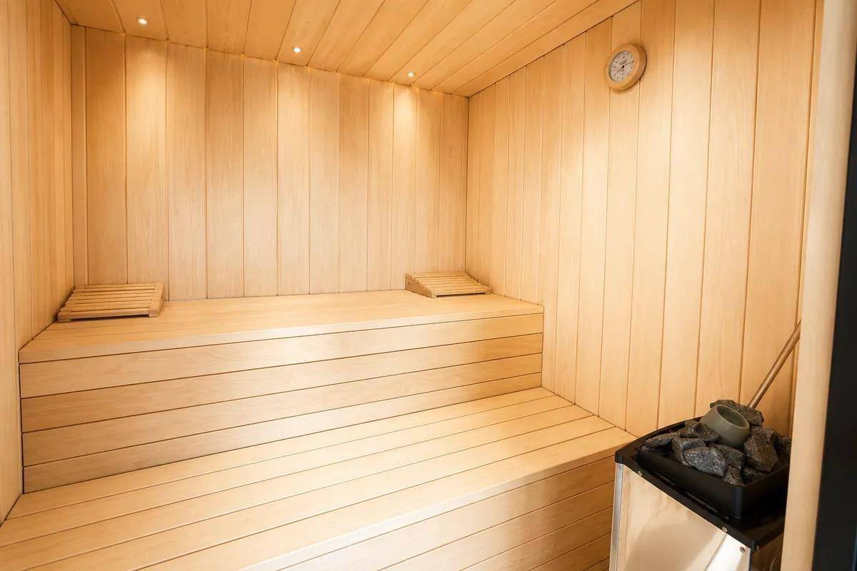 Innenansicht einer hellen Holzsauna mit Bänken und Saunaofen für Entspannung.