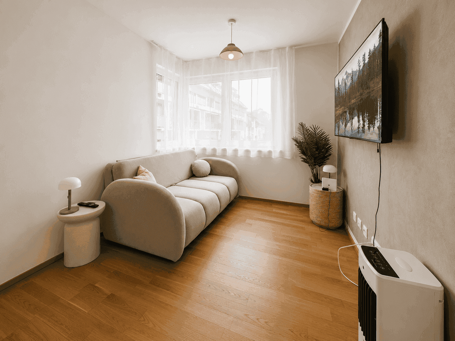 Heller Wohnbereich mit beigem Sofa, Holzboden und großem Fenster.
