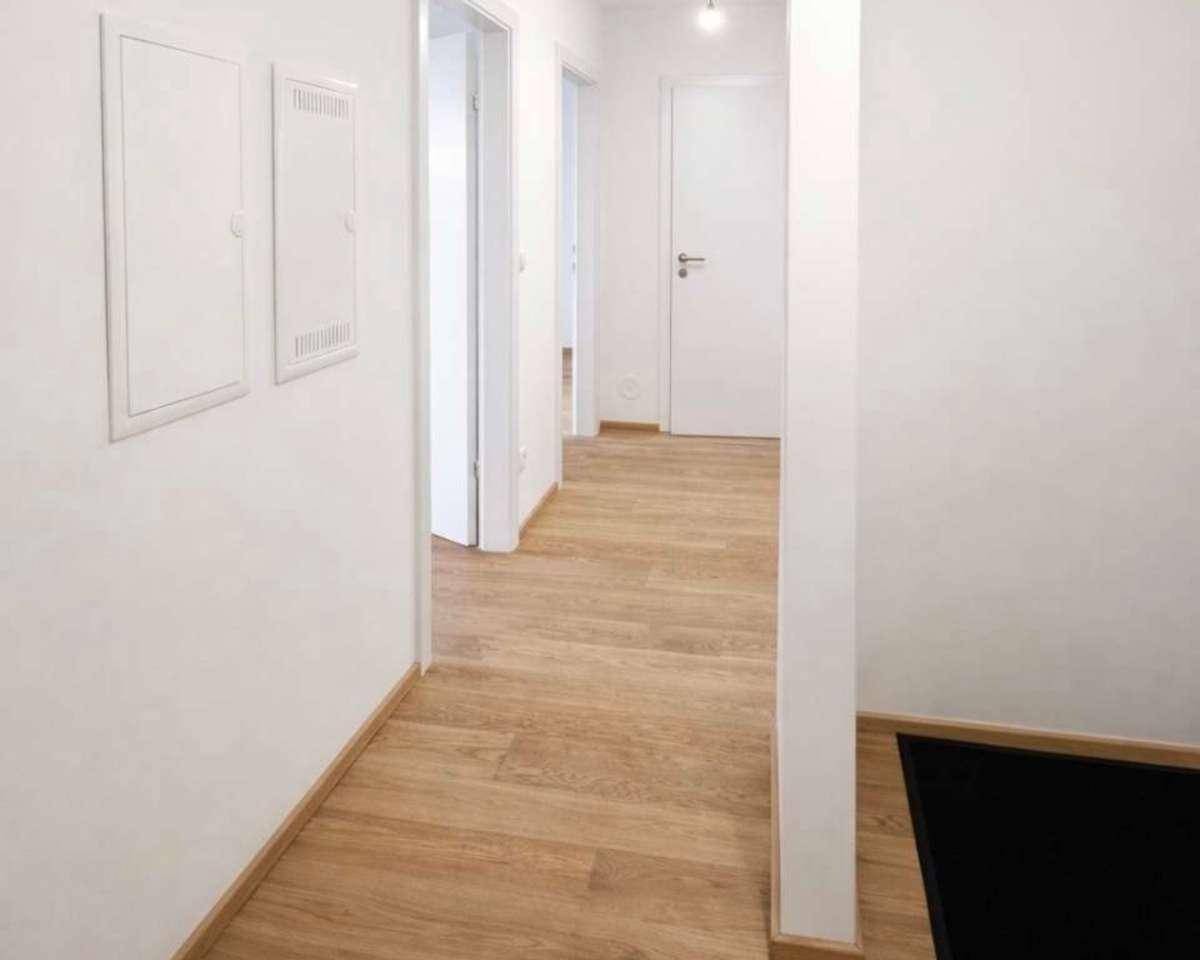 Heller Flur mit Holzfußboden und weißen Wänden, der zu verschiedenen Räumen im Haus führt.