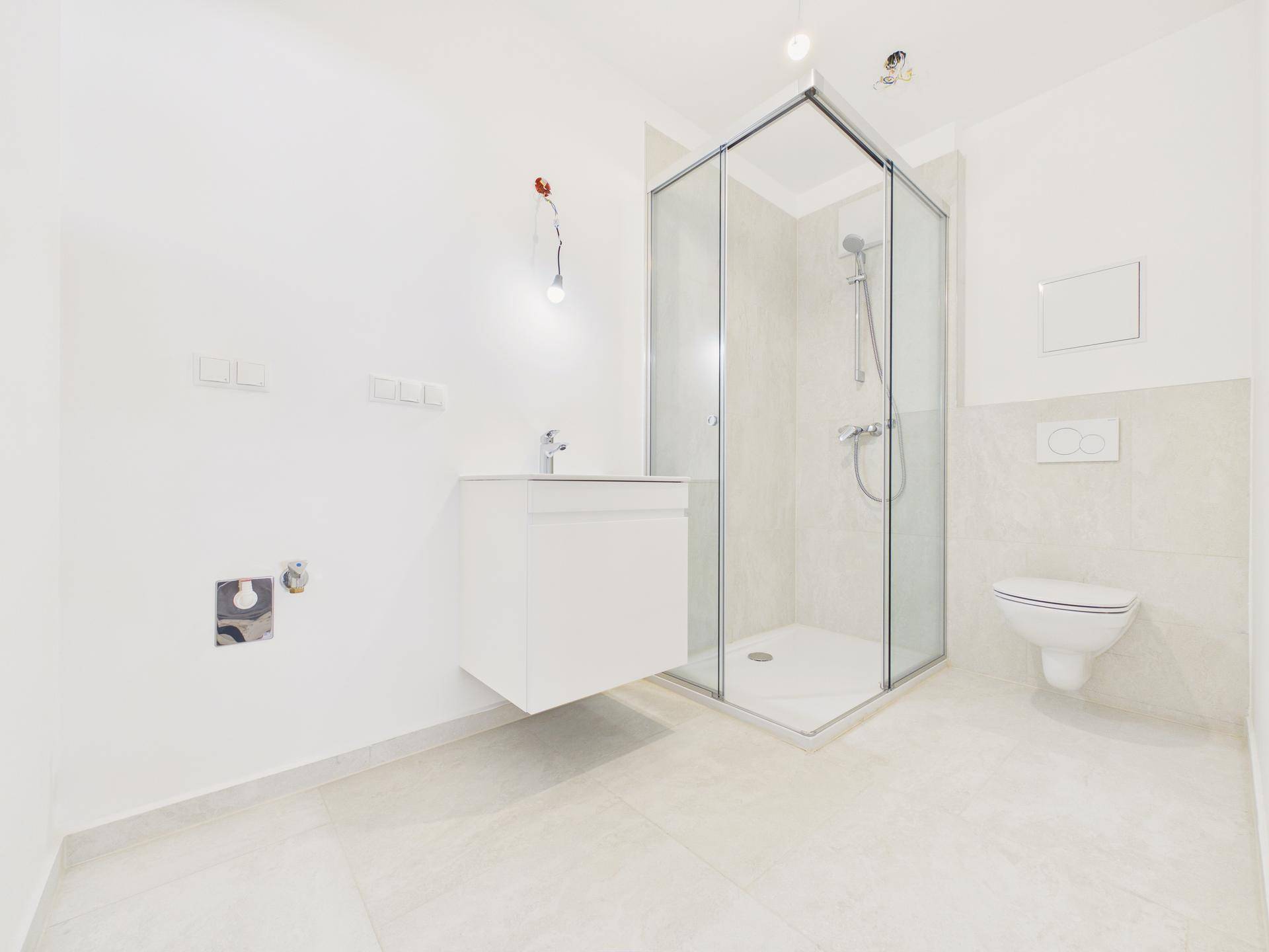 Modernes Badezimmer mit Duschkabine, Waschbecken und wandhängendem WC, hell gefliest.