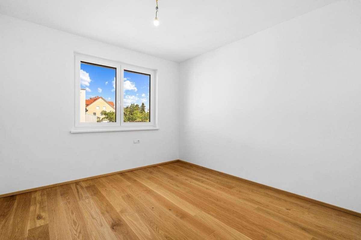 Unmöblierter Raum mit Holzboden und Fenster, das einen Blick ins Grüne bietet.