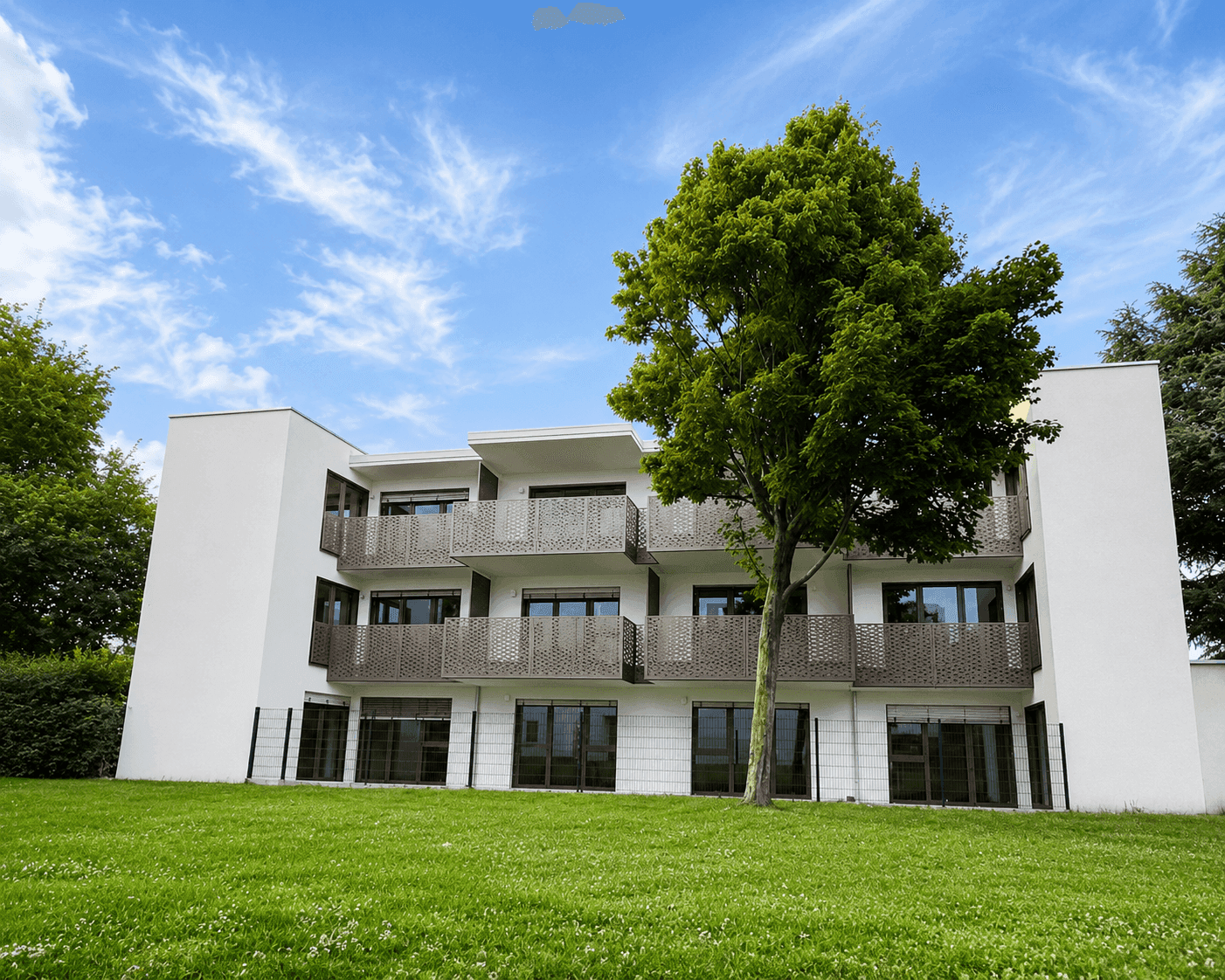 Modernes Wohngebäude mit Balkonen und einer großen Rasenfläche im Vordergrund unter blauem Himmel.