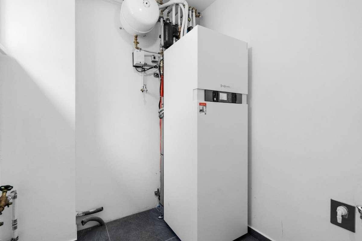 Technikraum mit Heizungsanlage und Warmwasserspeicher in weißer Ausführung.