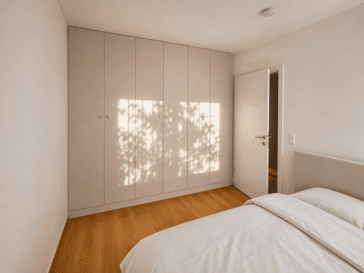 Helles Schlafzimmer mit Einbauschränken und Eichenparkett, durchflutet von natürlichem Licht.