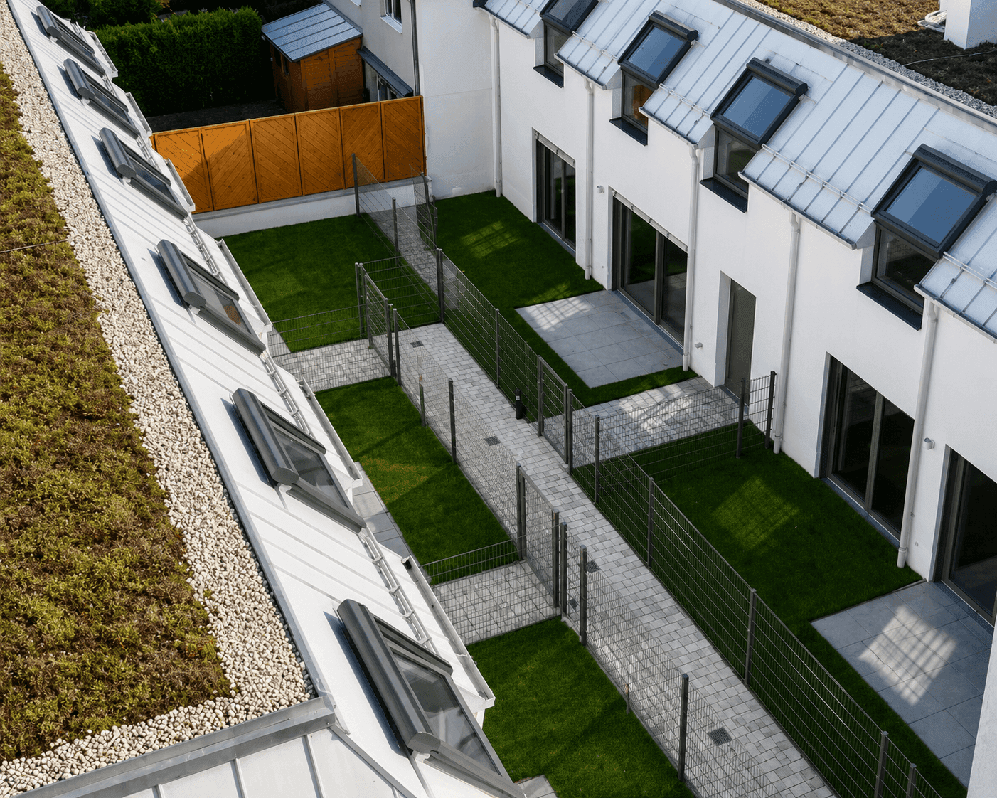 Blick von oben auf die privaten Gärten und gepflasterten Wege zwischen den modernen Wohngebäuden mit Gründach.
